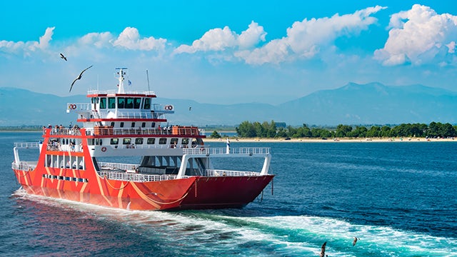 Large passenger ferry with white and blue exterior sailing on calm water against a cloudy sky