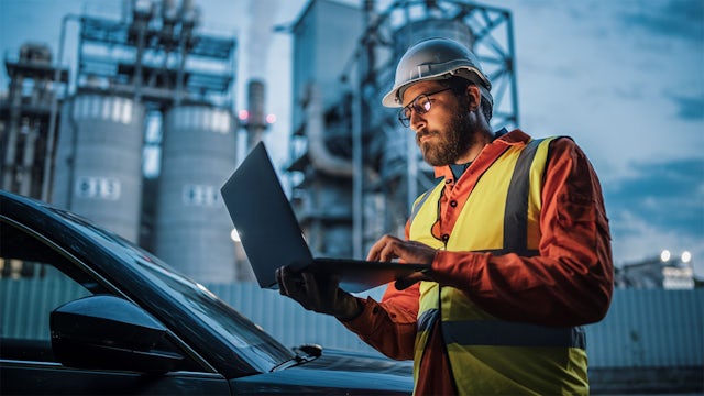 Man looking at laptop with power plant behind him.