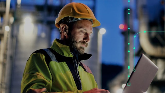 A technician is holding a tablet and is standing in front of industrial power equipment.
