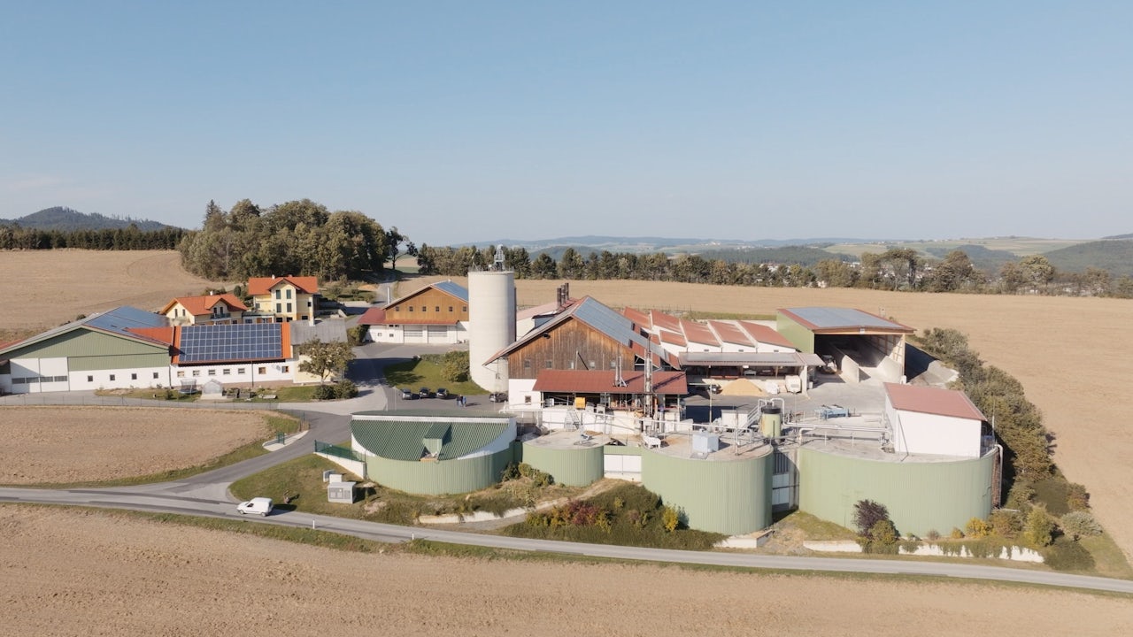 A person is standing in front of a Siemens logo, wearing a blue shirt and holding a Siemens product in their hand. 