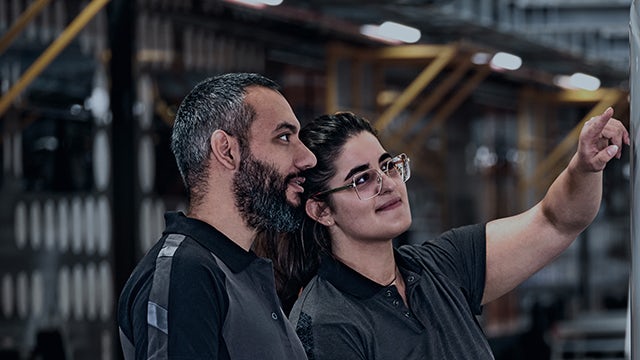 A group of people are standing together, smiling, and looking at the camera, possibly in a conference room.