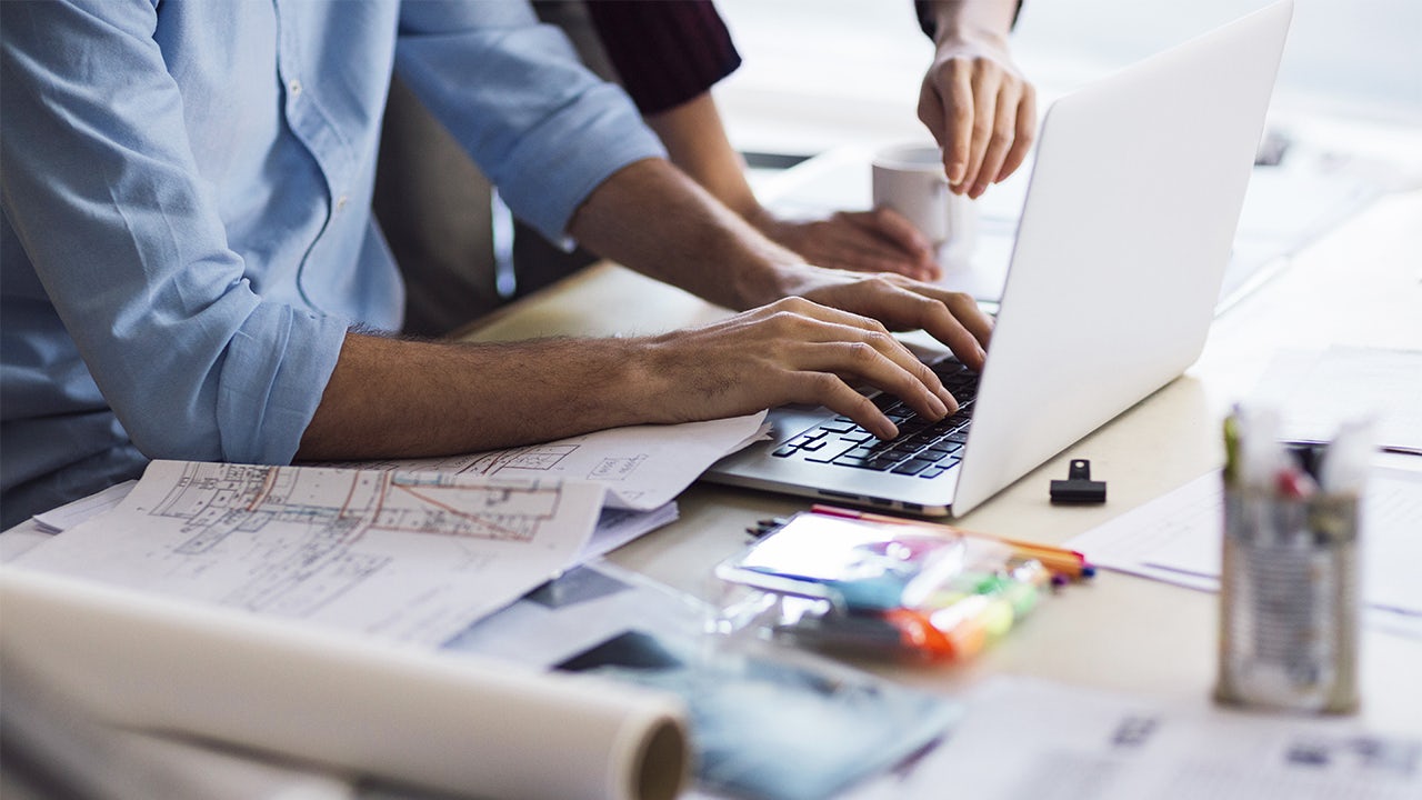 People are working on laptops in an office setting.