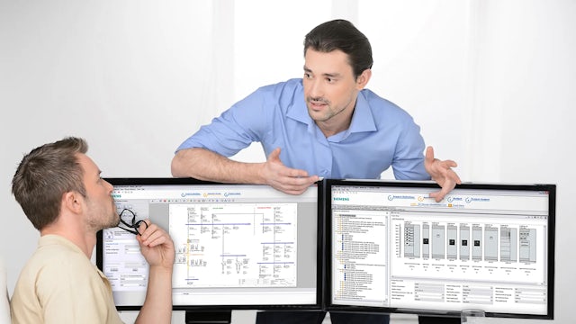 Two people having a discussion in front of two computer monitors.