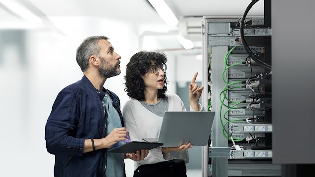 Two people standing in front of a computer server.