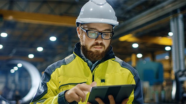 Man working in hard hat looking at a tablet in a warehouse.