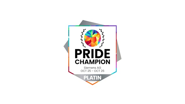 A person wearing a rainbow-colored shirt stands in front of a crowd, holding a flag and looking towards the camera.