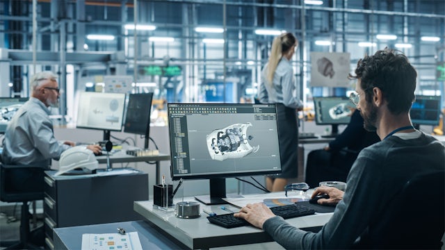 A person is working on a computer in a room with a desk and a window.