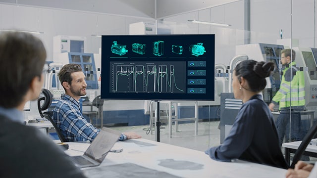 Three colleagues sitting at a table looking at data on a monitor.
