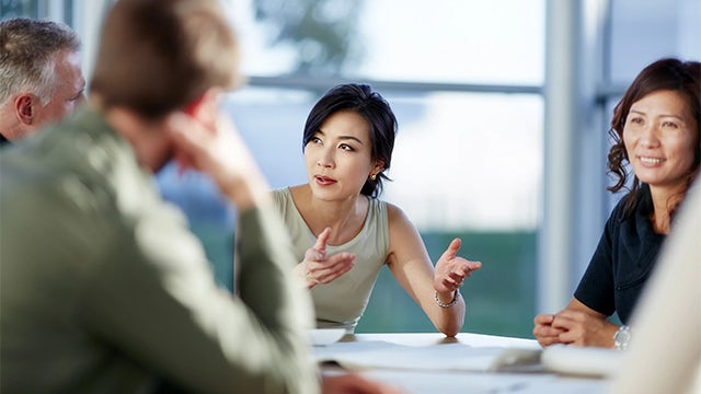 A woman in a business suit is sitting at a desk in an office, looking at a computer screen.