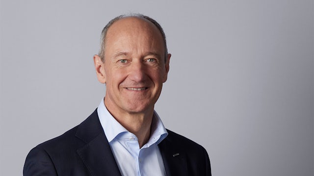 A man in a suit and tie is standing in front of a microphone, possibly giving a speech.