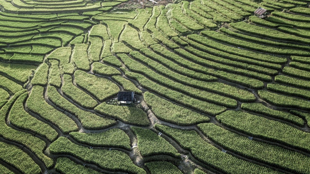 A rural landscape in Thailand with a city in the distance, surrounded by trees and mountains. 