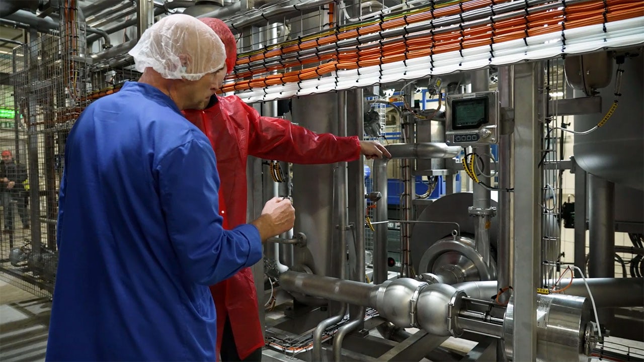 Two workers at a dairy factory inspecting the machinery.