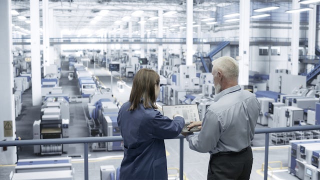A male engineer and a female Asian scientist using a laptop and talking in a factory facility.