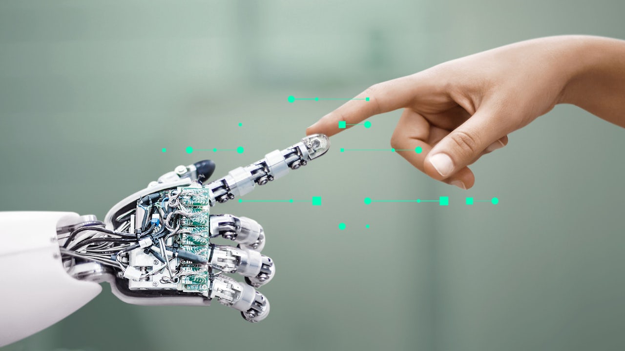 A robot hand reaches out to touch the finger of a human hand. 