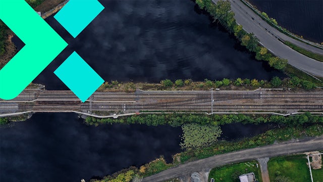 Birds-eye view of train tracks next to trees and water.