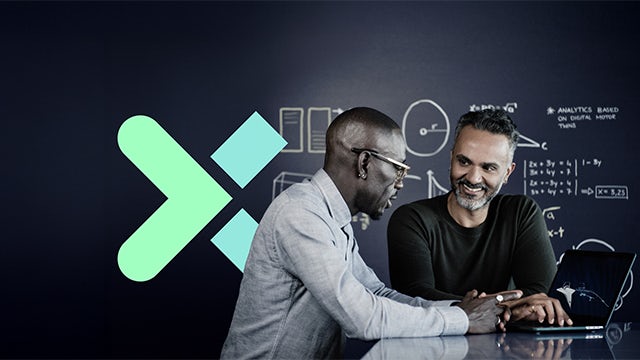 Two men collaborate in front of a chalkboard-style wall with diagrams with the Siemens Xcelerator "X" logo in the background.