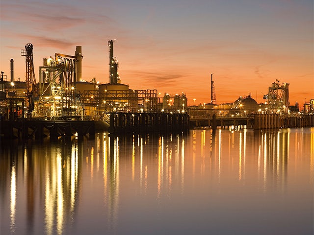 Industrial complex with lights reflecting on water at sunset, showcasing infrastructure and calm water.