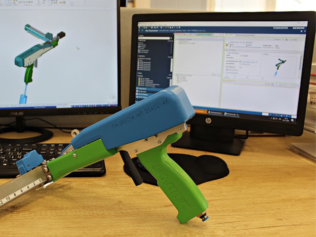 Person in black shirt standing against white wall with black border, holding a dark object.