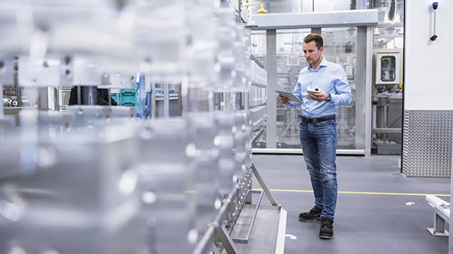 Man in jeans in a manufacturing plant looking at a tablet