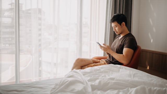 A hotel room with a modern interior design, featuring a bed, a desk, and a window with a city view.