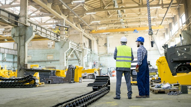 Two heavy equipment manufacturing workers assessing machines.