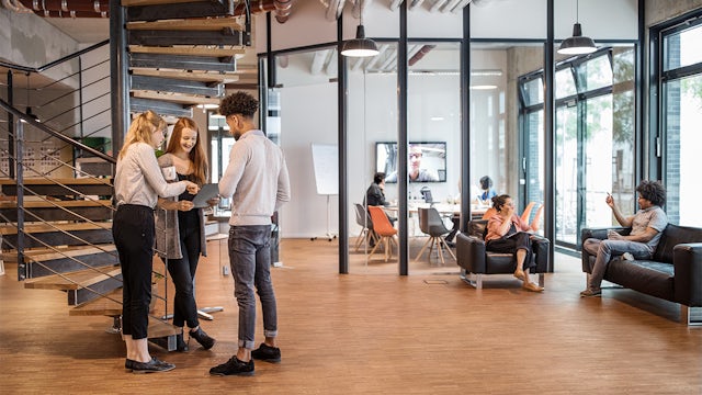 A modern office space with a desk, computer, and a person working on a laptop.