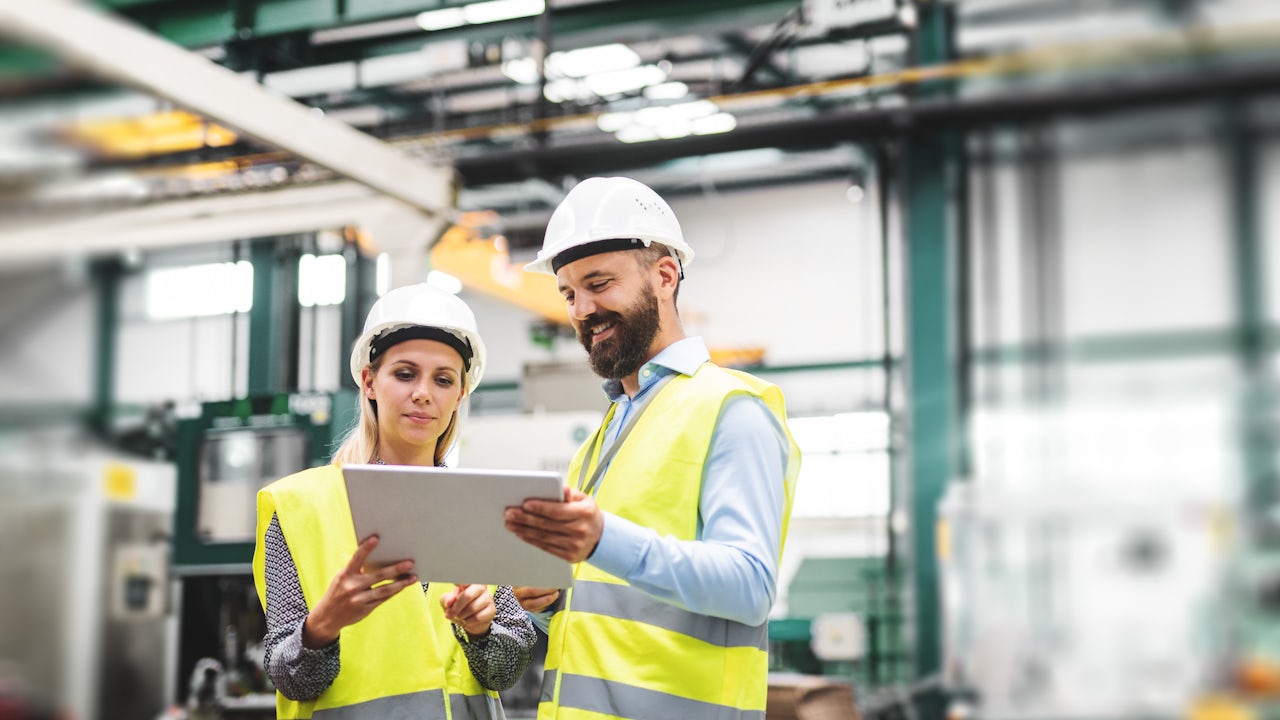 A factory with workers using tablets and a large table with various items on it.