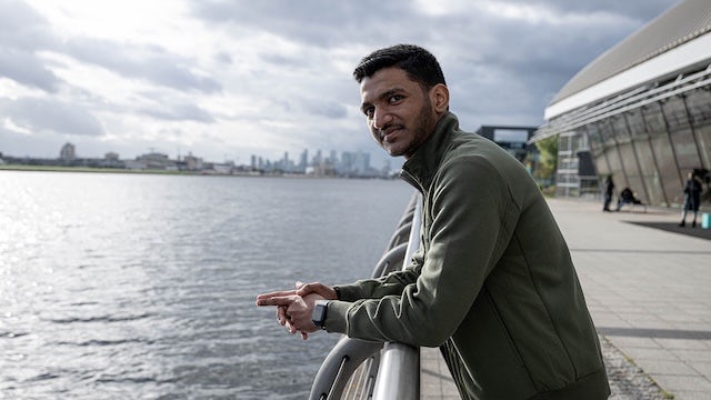 A man is standing on a bridge, looking out at a cityscape.