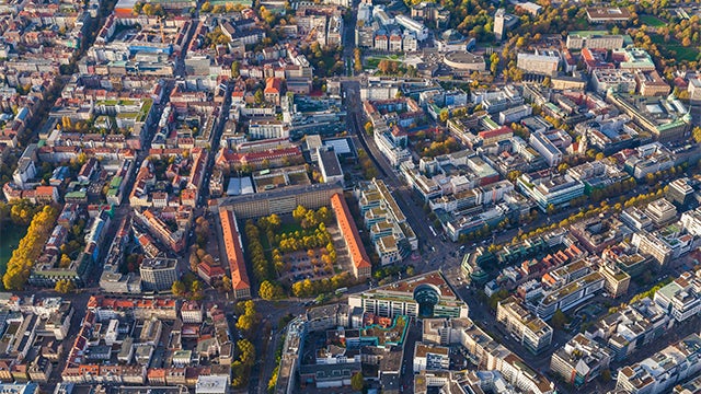 A city street with a modern building featuring a large digital display and a person walking on the sidewalk.