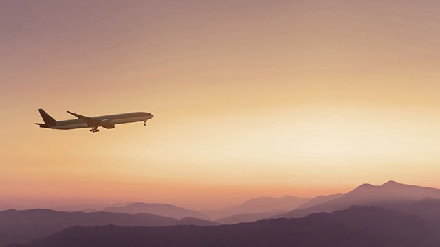 Airplane flying in front of a sunset and clouds.
