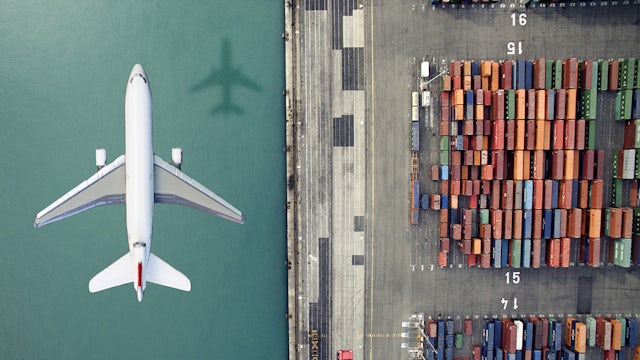 The image shows a plane flying over cargo containers in the water.