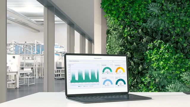 A laptop displaying energy management analytics on a table in a green production facility