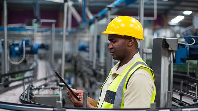 Person wearing safety glasses and hardhat examining a machine part in an industrial setting