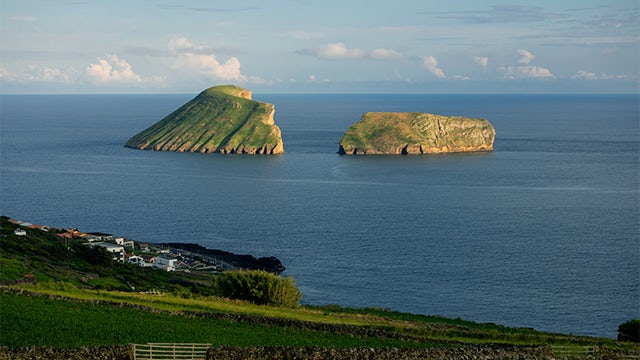 A scenic view of Terceira Island in the Azores Archipelago with a rocky coastline and a clear blue sky.