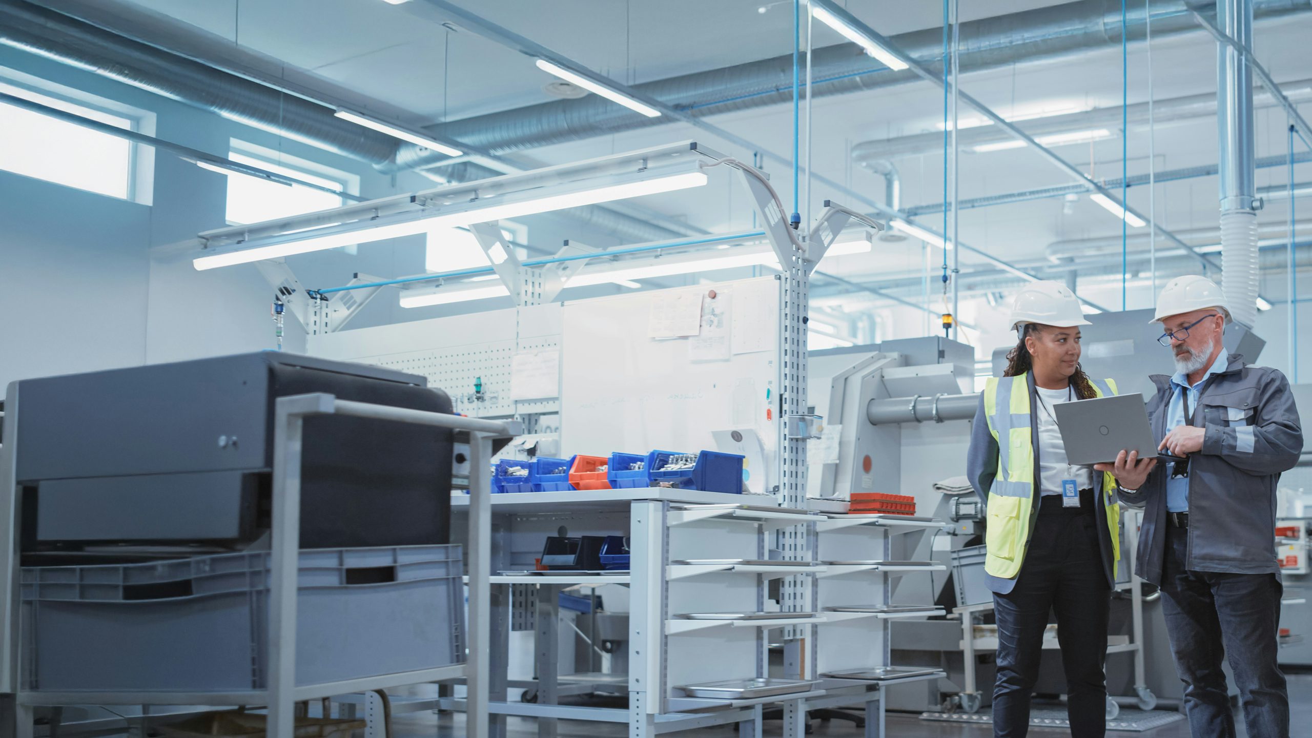 Two engineers in hard hats standing in factory looking at a laptop.
