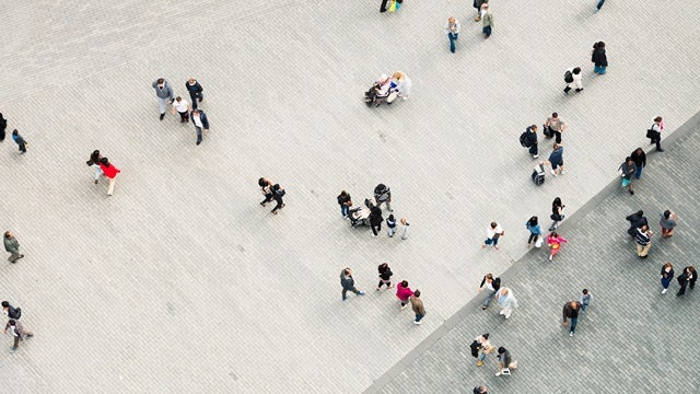 Aerial view of a crowded urban street with pedestrians walking between buildings in a city center.