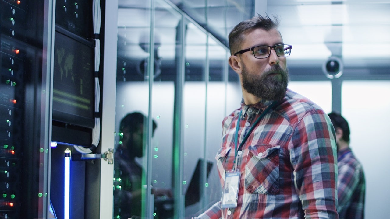 A man in a plaid shirt works in a data center.