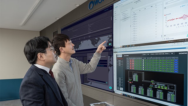 A person's hand holding a white paper document against a blurred background of office desks and chairs.