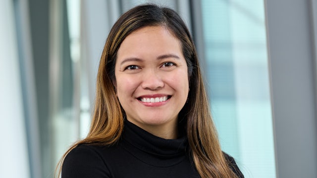 Woman with short hair in white shirt and black jacket standing near window against white wall