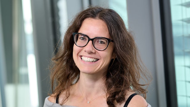 Woman with short hair wearing a white shirt standing in front of a white wall.