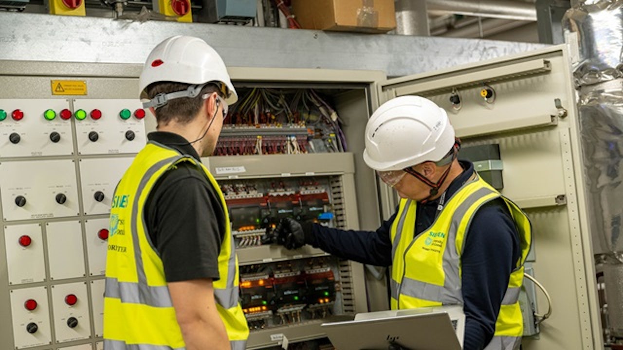Two workers in safety equipment monitoring the building management system at University of East London.