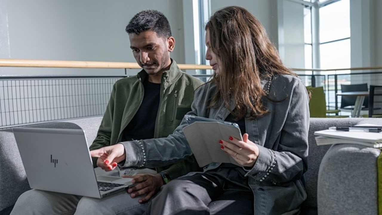 Two University of East London students consult a laptop and tablet in a study area.